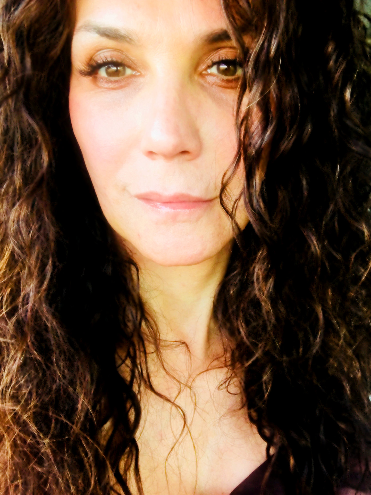 Gabriela, trans life coach, with curly brunette hair and natural makeup, in a soft light portrait for BetterSelf Coaching.